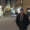 Man in hoodie and beanie smiling, brick street and buildings in the background 